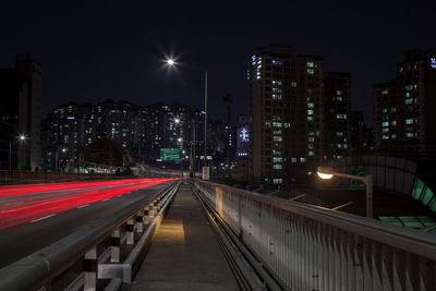 Light trails on bridge leading towards buildings in at night