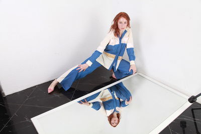 Fashion portrait of stylish woman in summer blue white stripes suit  sitting near reflecting mirror