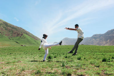 Full length of woman kicking man on field against sky during sunny day