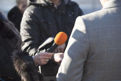 Midsection of journalists interviewing businessman while standing outdoors