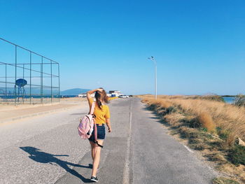 Woman with umbrella on road against clear sky