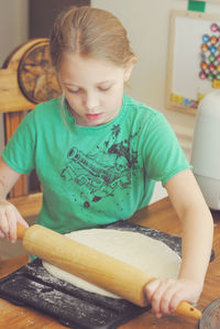 Girl rolling dough for pizza at table