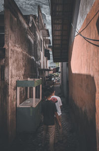 Rear view of woman standing on alley amidst buildings