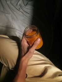 Hand holding orange juice in a small glass jar 