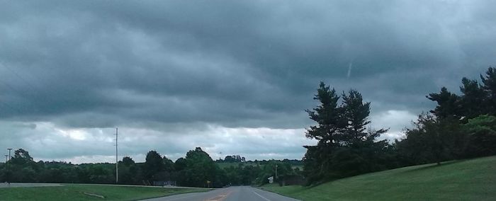 Road passing through field against cloudy sky