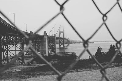 Chainlink fence against bridge in city against sky