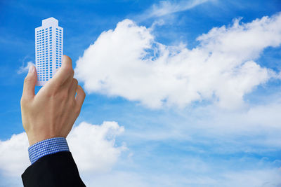 Cropped of business person holding model building against cloudy sky