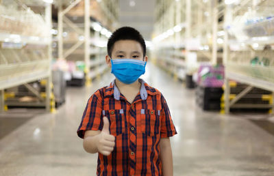 Portrait of cute boy with mask showing thumb standing in factory