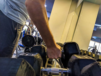 Midsection of man holding dumbbell while standing in gym