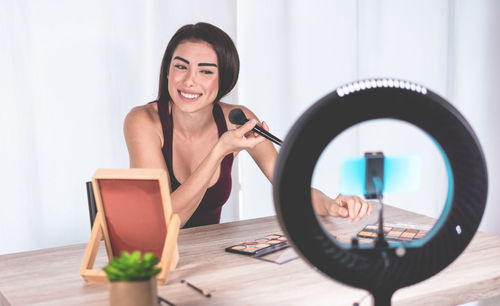 Female blogger applying make-up while filming over smart phone at home