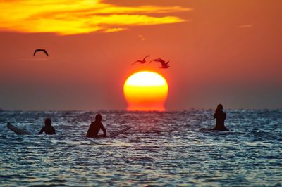 Silhouette people on beach against orange sky