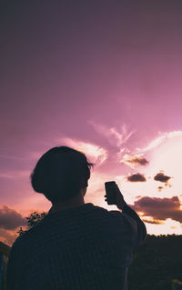 Rear view of silhouette man photographing against sky during sunset