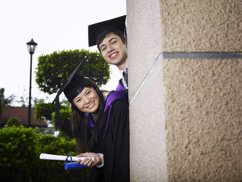 Portrait of smiling friends wearing mortarboard by wall