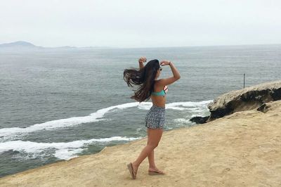 Rear view of woman standing at beach against sky