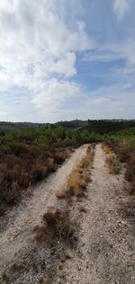 Dirt road in field against cloudy sky