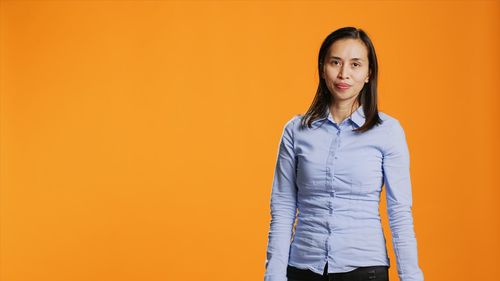 Portrait of young woman standing against yellow background