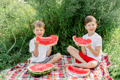 Portrait of smiling kids eating watermelon while sitting against plants