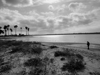 Full length of man walking at beach against cloudy sky