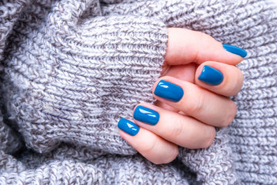 Stylish women's manicure in blue on the background of a knitted gray jacket.