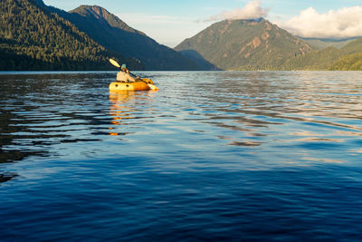 Young man paddling on lake towards mountain at sunset