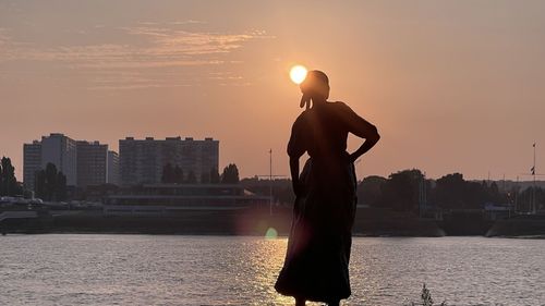 Man standing by river against sky during sunset