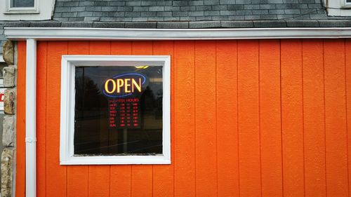 Close-up of open sign on orange wall of shop