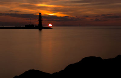 Silhouette lighthouse by sea against sky during sunset