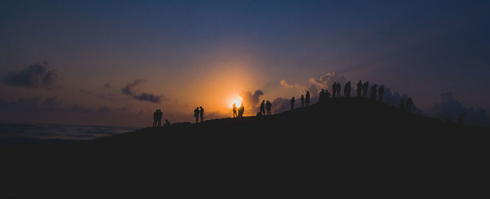 Silhouette people on beach against sky during sunset