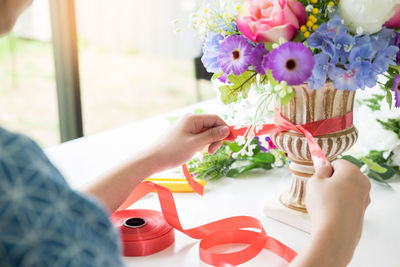 Midsection of woman tying ribbon on flower vase at home