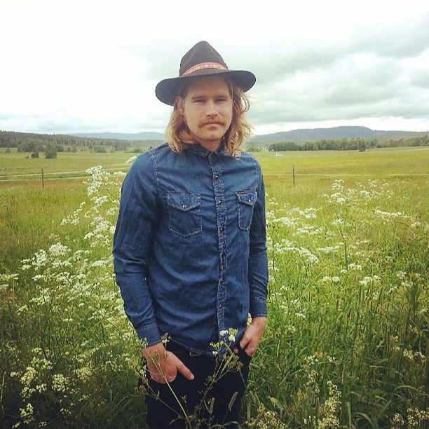 field, landscape, casual clothing, lifestyles, sky, leisure activity, standing, person, portrait, grass, looking at camera, rural scene, three quarter length, front view, young adult, nature, agriculture, mountain