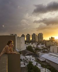 Thoughtful woman standing at building terrace by cityscape during sunset