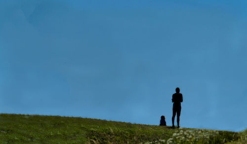 Rear view of man walking on field against blue sky