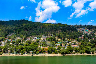 Scenic view of river by trees and cityscape against sky