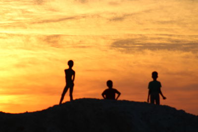 Silhouette children playing against sky during sunset