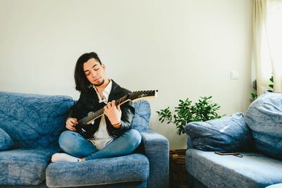Man playing guitar while sitting on sofa