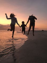 Full length of men jumping on beach against sky during sunset