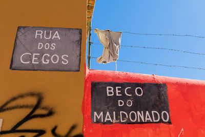 Low angle view of text and graffiti on wall against clear sky