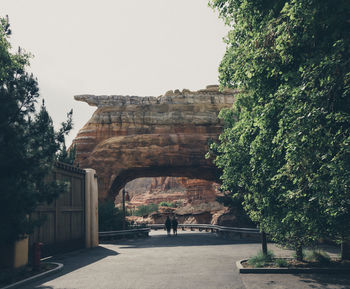 People walking below natural rock arch against sky