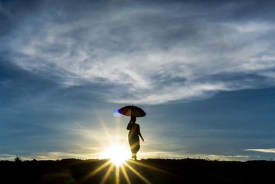 Silhouette woman standing on field against sky during sunset