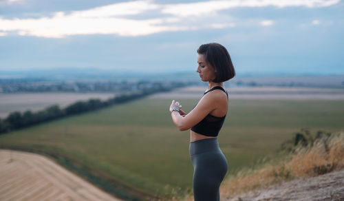 Side view of young woman exercising on field against sky