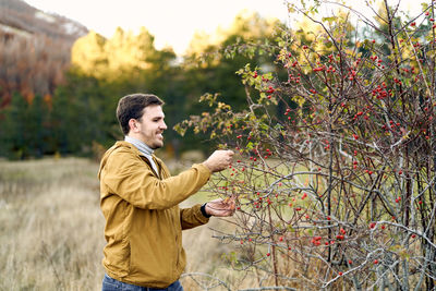 Side view of young man standing against trees