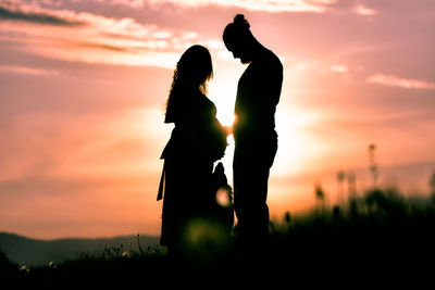 Silhouette woman standing on field against sky during sunset