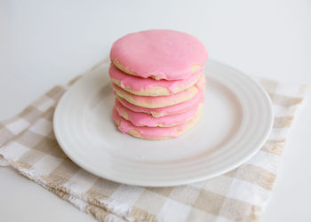 Stack of pink frosted sugar cookies on white plate with neutral colors