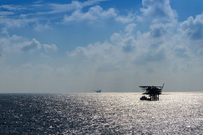 Silhouette oil drill amidst sea against sky