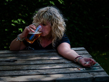 Woman drinking beer while holding pills on table