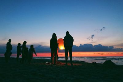 Silhouette people standing at beach against sky during sunset