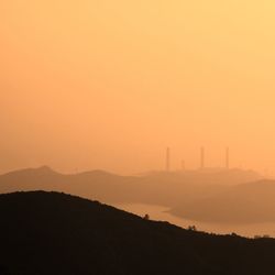 Silhouette smoke emitting from factory against orange sky