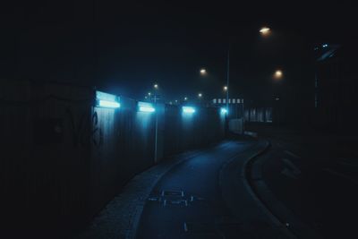Empty road along illuminated street lights at night