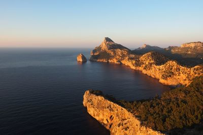 Scenic view of sea by mountain against clear sky