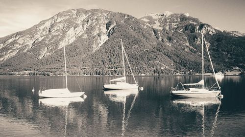 Sailboats moored in lake by snowcapped mountains against sky